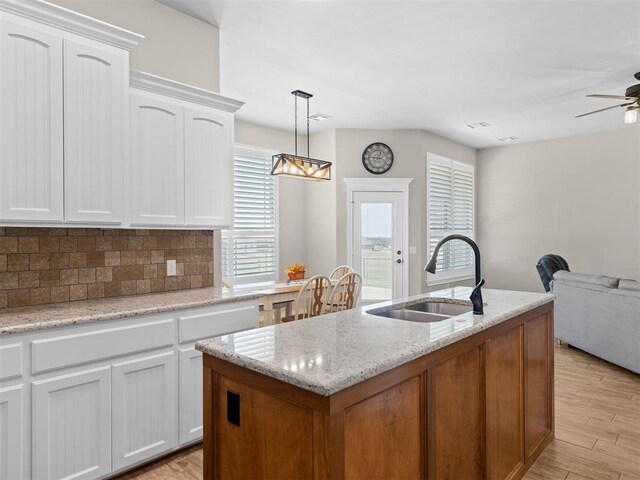 kitchen featuring sink, hanging light fixtures, a center island with sink, white cabinets, and light wood-type flooring