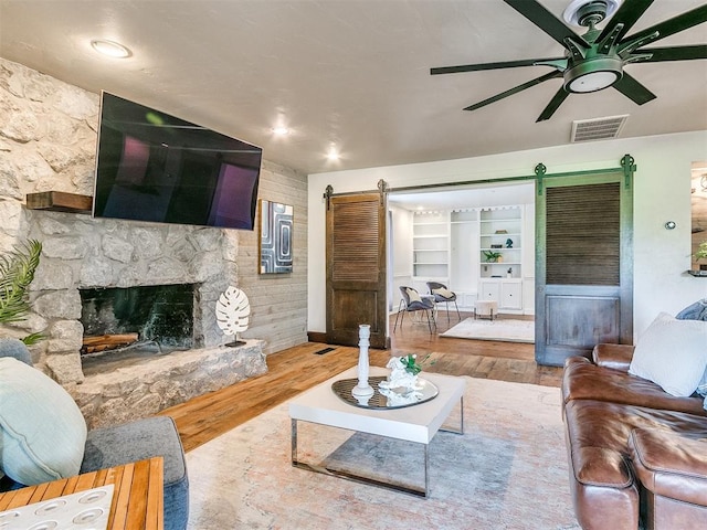 living room with a stone fireplace, built in features, a barn door, and hardwood / wood-style flooring