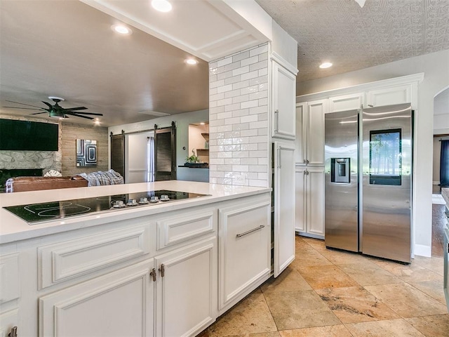 kitchen featuring stainless steel refrigerator with ice dispenser, backsplash, black electric cooktop, a barn door, and white cabinets