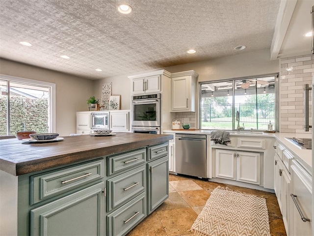 kitchen with a center island, stainless steel appliances, butcher block countertops, decorative backsplash, and white cabinets