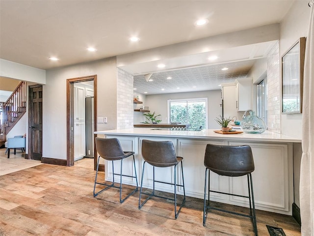 kitchen with a breakfast bar area, kitchen peninsula, white cabinetry, and light wood-type flooring