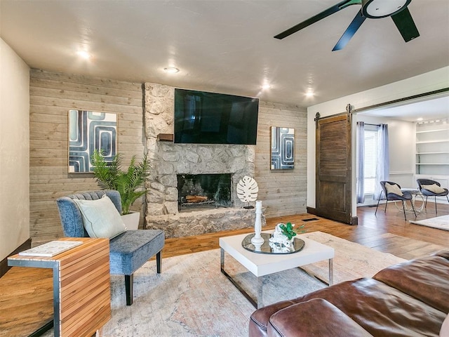 living room featuring wood-type flooring, a stone fireplace, and wooden walls