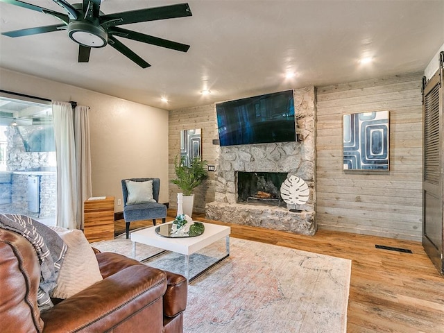 living room featuring hardwood / wood-style flooring, a stone fireplace, ceiling fan, and wooden walls