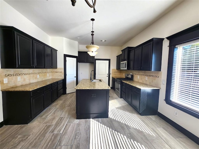 kitchen featuring backsplash, a kitchen island with sink, sink, decorative light fixtures, and stainless steel appliances