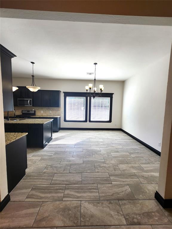 kitchen featuring a chandelier, appliances with stainless steel finishes, light stone countertops, and hanging light fixtures