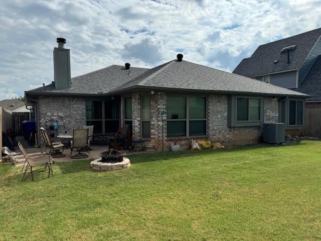 rear view of house with a fire pit, cooling unit, and a lawn