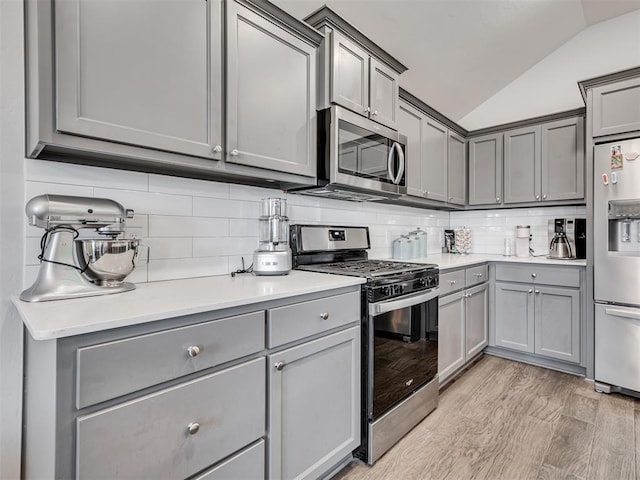 kitchen with gray cabinetry, backsplash, light hardwood / wood-style flooring, vaulted ceiling, and stainless steel appliances