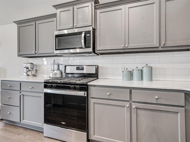 kitchen with light wood-type flooring, stainless steel appliances, gray cabinets, and tasteful backsplash