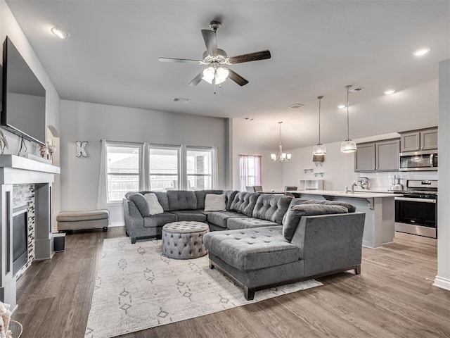 living room with hardwood / wood-style floors, ceiling fan with notable chandelier, and a stone fireplace