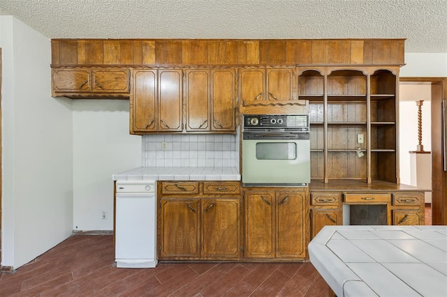 kitchen with dark hardwood / wood-style flooring, backsplash, tile countertops, oven, and a textured ceiling