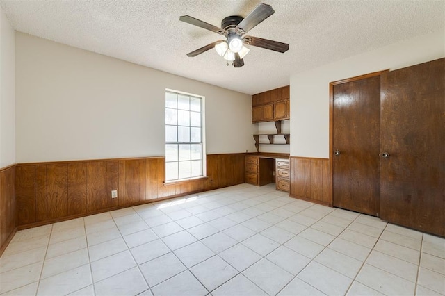 interior space with wooden walls, ceiling fan, light tile patterned floors, built in desk, and a textured ceiling