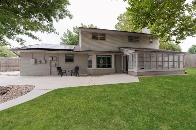 rear view of house with a sunroom, solar panels, a patio area, and a yard