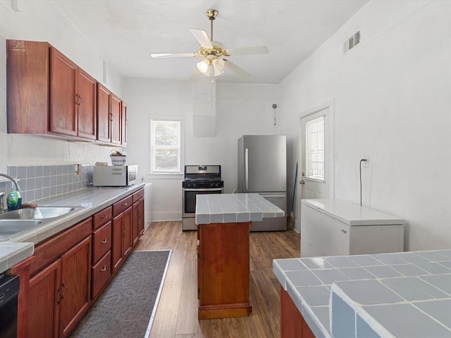 kitchen featuring sink, a wealth of natural light, appliances with stainless steel finishes, tile counters, and a kitchen island