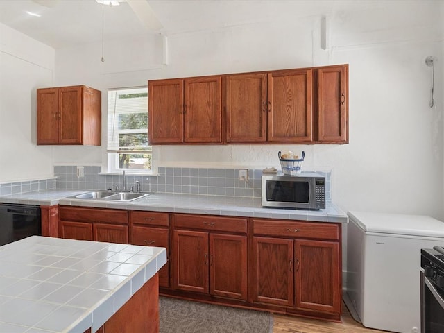 kitchen with decorative backsplash, stainless steel appliances, sink, light hardwood / wood-style floors, and tile counters