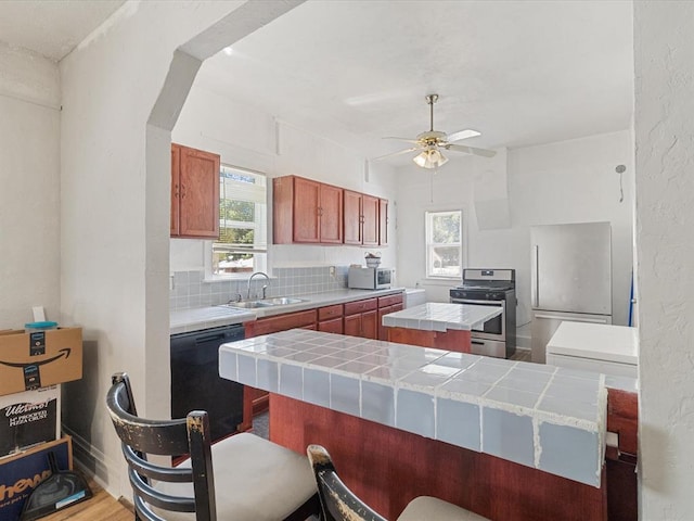 kitchen featuring tile countertops, a wealth of natural light, sink, and appliances with stainless steel finishes