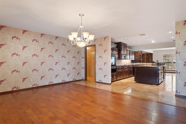 kitchen with pendant lighting, a kitchen island with sink, wall oven, dark brown cabinets, and light wood-type flooring