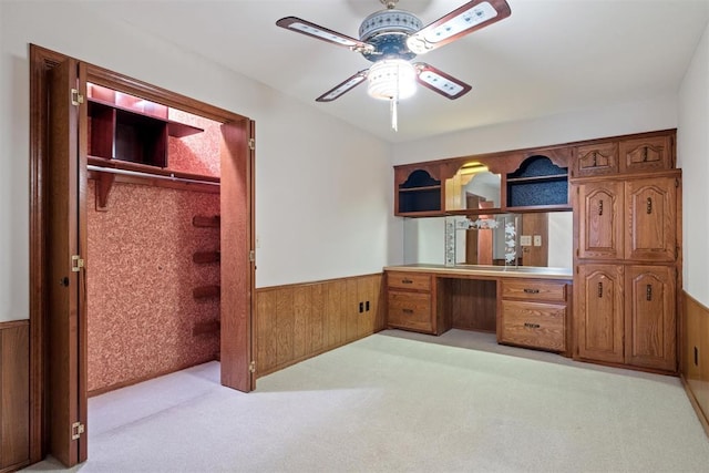 office featuring light carpet, built in desk, ceiling fan, and wood walls