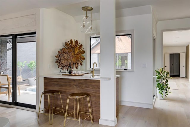 bar with light wood finished floors, hanging light fixtures, baseboards, and a sink