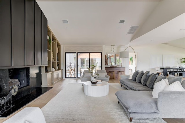 living room with built in features, lofted ceiling, a premium fireplace, and light wood-type flooring