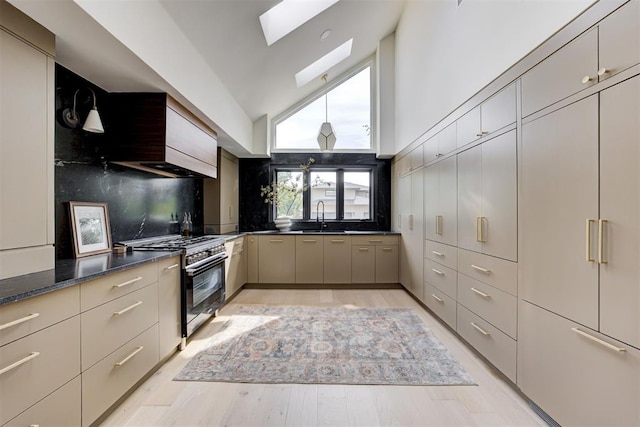 kitchen with a skylight, light wood-style flooring, a sink, high end stove, and backsplash