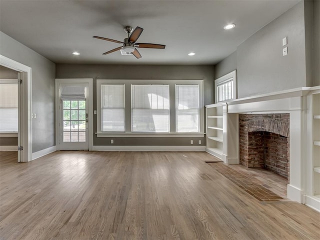 unfurnished living room with a fireplace, built in shelves, light wood-type flooring, and ceiling fan