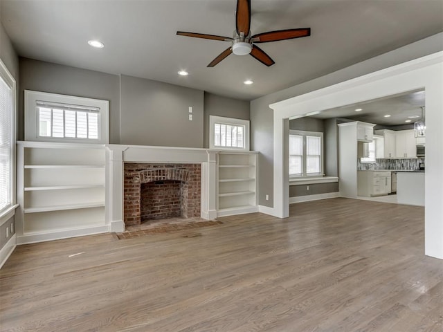 unfurnished living room featuring ceiling fan, light hardwood / wood-style flooring, and a brick fireplace