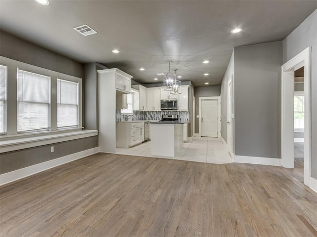 kitchen featuring backsplash, light hardwood / wood-style flooring, decorative light fixtures, a kitchen island, and white cabinetry