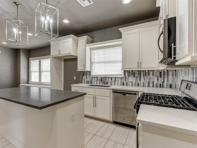 kitchen featuring appliances with stainless steel finishes, sink, white cabinets, a kitchen island, and hanging light fixtures