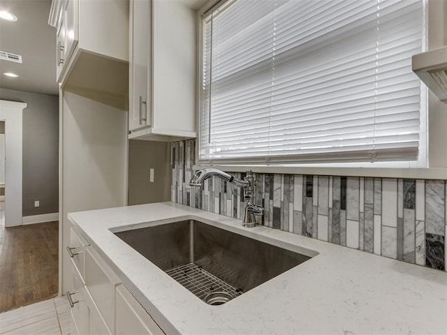 kitchen featuring light stone countertops, white cabinetry, a healthy amount of sunlight, and sink