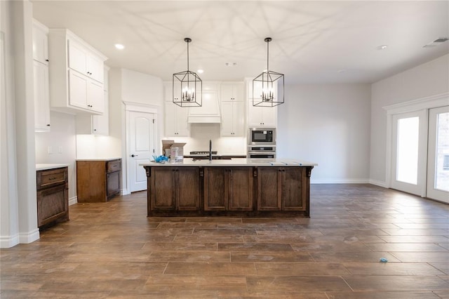 kitchen with oven, white cabinetry, a center island with sink, pendant lighting, and built in microwave