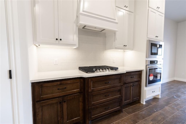 kitchen featuring stainless steel appliances, custom range hood, white cabinetry, and tasteful backsplash