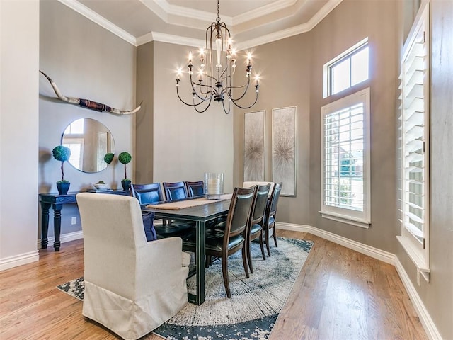 dining area featuring a raised ceiling, light hardwood / wood-style flooring, a notable chandelier, and crown molding