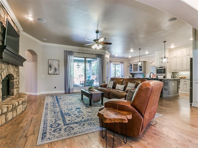 living room featuring a stone fireplace, ceiling fan, light hardwood / wood-style flooring, and ornamental molding