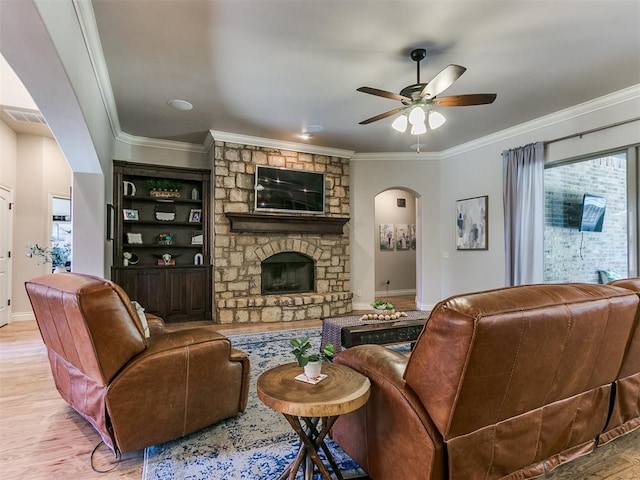 living room featuring light hardwood / wood-style flooring, a stone fireplace, ceiling fan, and crown molding