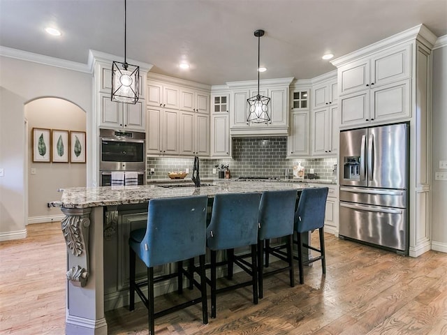 kitchen featuring stainless steel appliances, light stone counters, crown molding, decorative light fixtures, and a kitchen island with sink