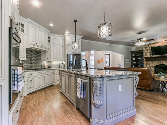 kitchen with light stone countertops, stainless steel appliances, pendant lighting, a center island with sink, and white cabinets