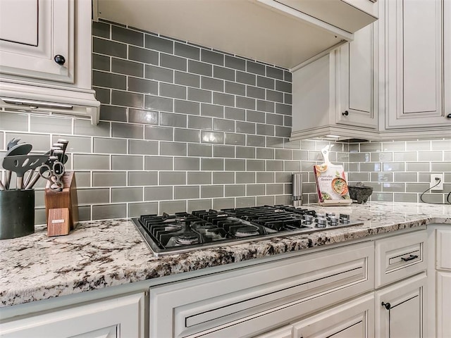 kitchen featuring tasteful backsplash, light stone counters, white cabinets, and stainless steel gas cooktop