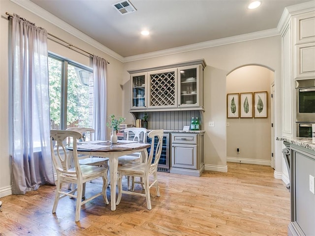 dining room with light hardwood / wood-style floors, wine cooler, and ornamental molding