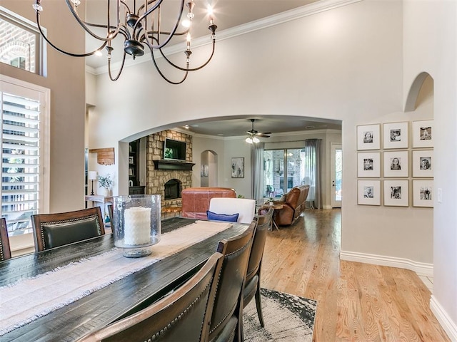 dining space with ceiling fan with notable chandelier, light hardwood / wood-style floors, a stone fireplace, and crown molding