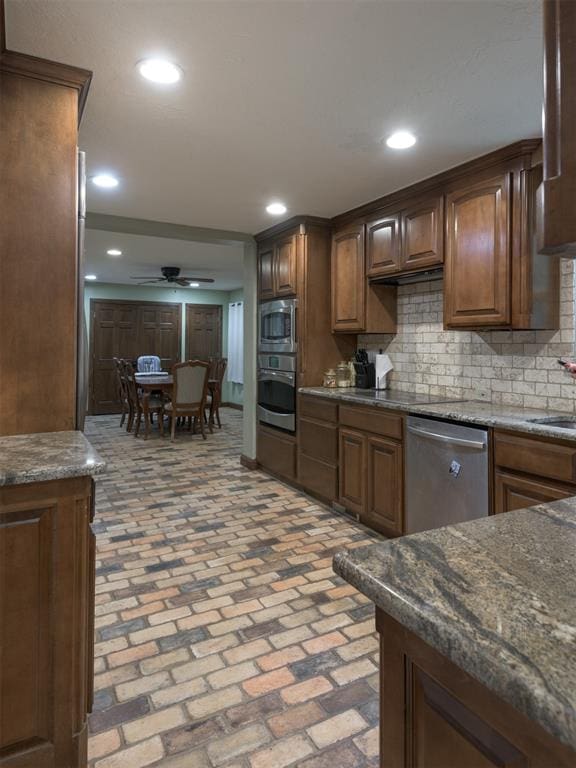 kitchen featuring dark stone countertops, decorative backsplash, stainless steel appliances, and ceiling fan