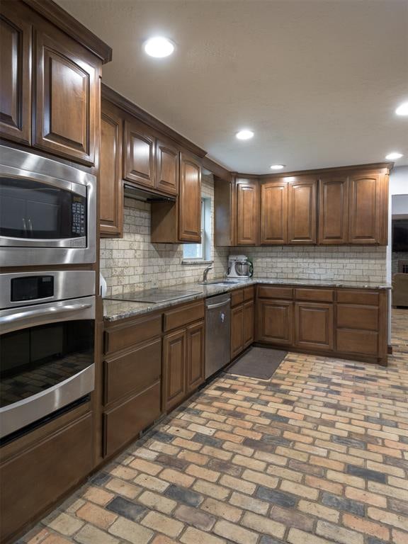 kitchen with light stone counters, sink, tasteful backsplash, and appliances with stainless steel finishes