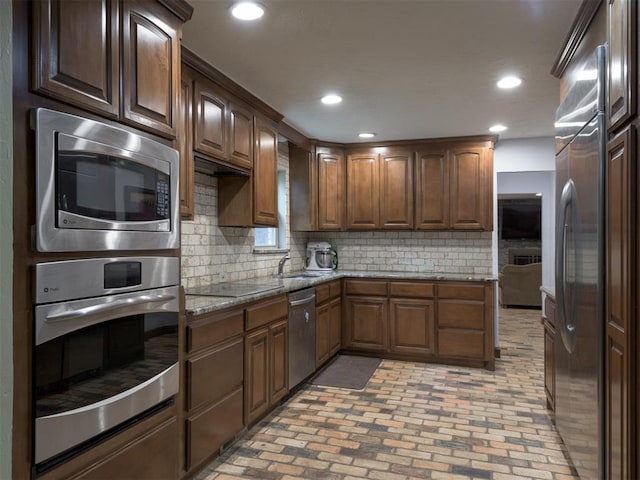 kitchen with tasteful backsplash, appliances with stainless steel finishes, stone countertops, and sink