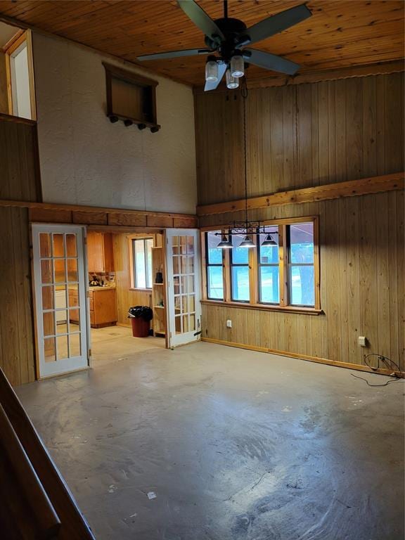 unfurnished living room featuring ceiling fan, a towering ceiling, wood ceiling, and wooden walls