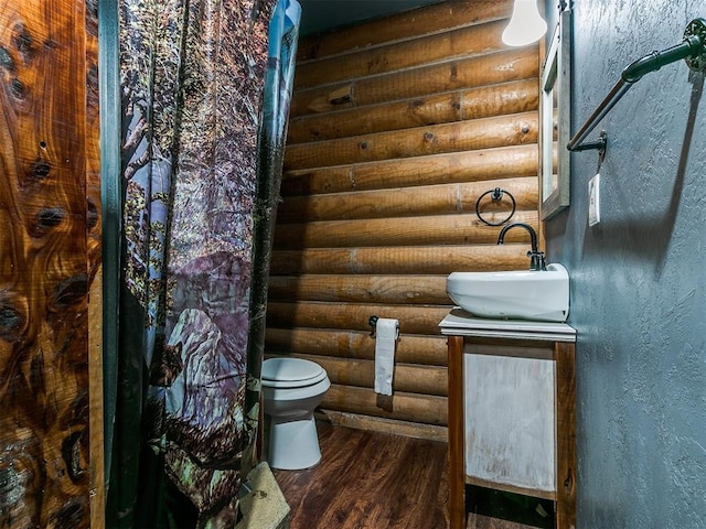 bathroom with toilet, hardwood / wood-style floors, rustic walls, and sink