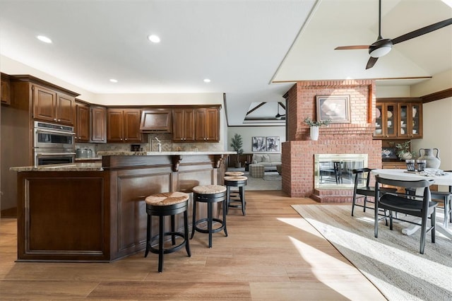 kitchen featuring backsplash, ceiling fan, dark stone countertops, stainless steel double oven, and custom range hood