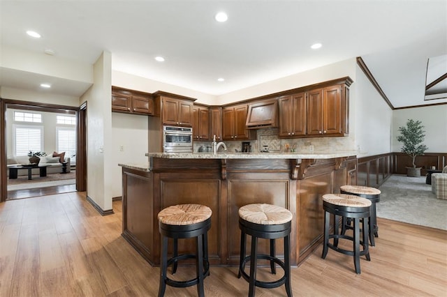 kitchen featuring oven, kitchen peninsula, custom range hood, and a breakfast bar area