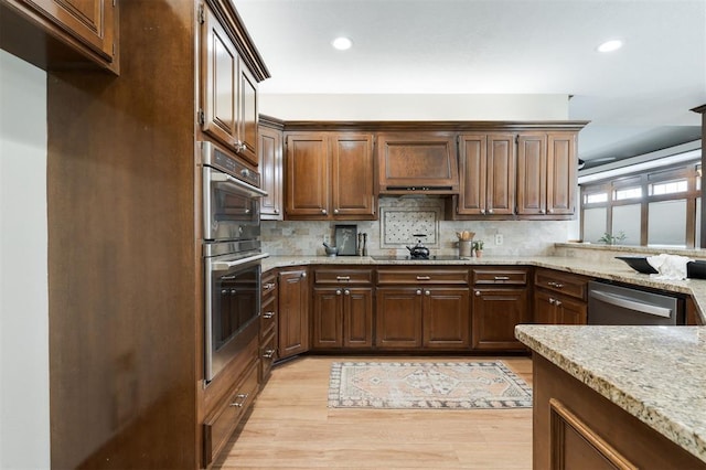 kitchen featuring tasteful backsplash, light stone countertops, light hardwood / wood-style floors, and appliances with stainless steel finishes