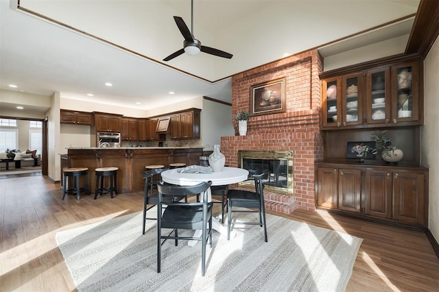 dining room with light hardwood / wood-style floors, a brick fireplace, and ceiling fan