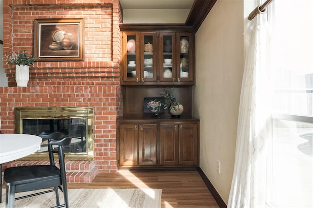 interior space featuring dark brown cabinets, light wood-type flooring, a brick fireplace, and ornamental molding