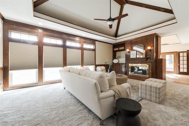 carpeted living room with a raised ceiling, ceiling fan, a fireplace, and crown molding